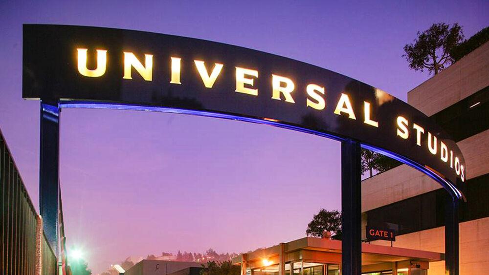 Illuminated "Universal Studios" sign. Buildings and sunset behind it.