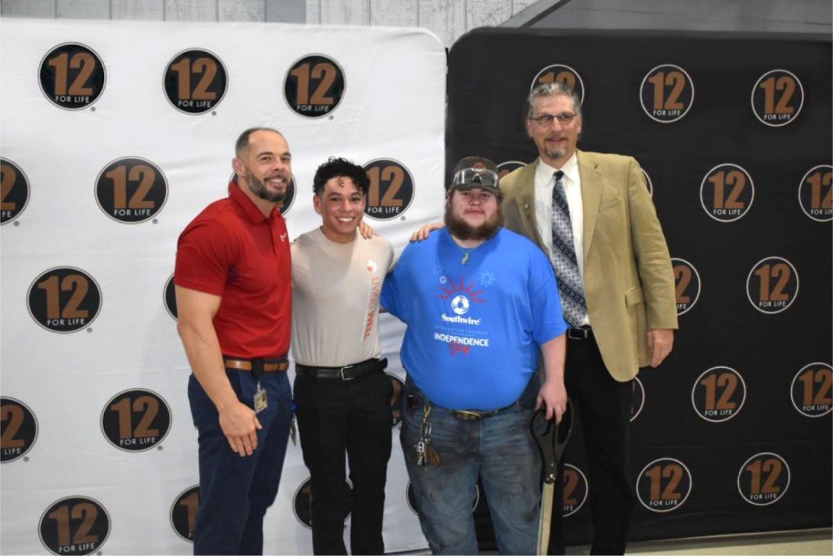 Four people stood next to each other smiling with a 12 for Life®  backdrop behind them