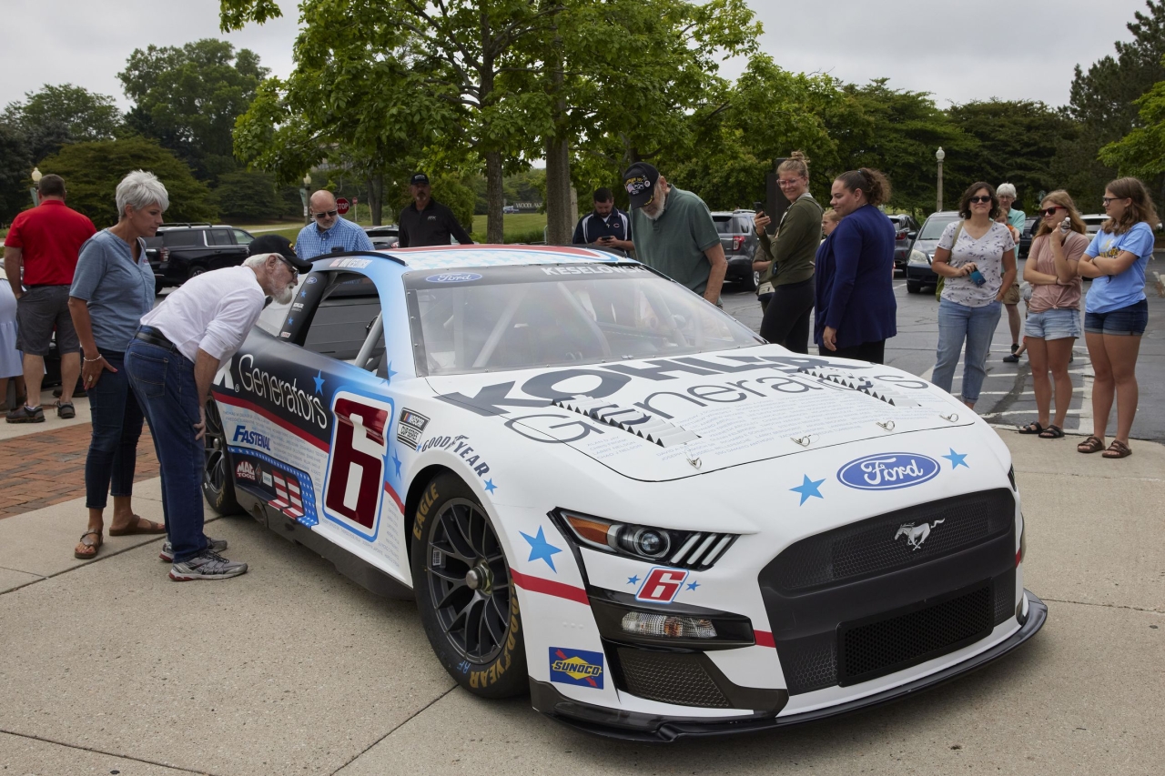 a group of people around a race car, some look in the windows