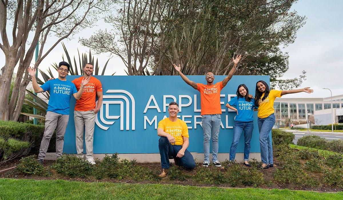 group smiling in front of Applied Materials logo