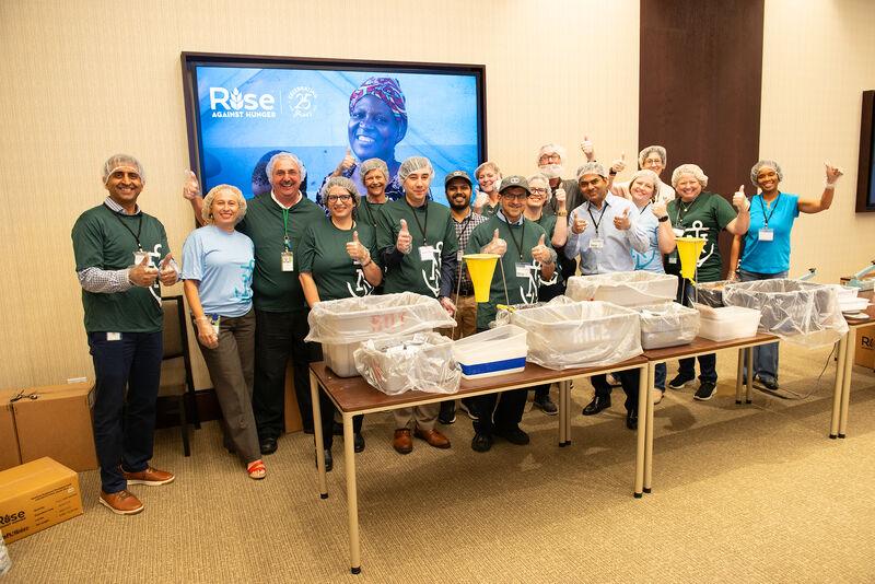 Group of volunteers posed, giving thumbs-up, behind a table of bins.