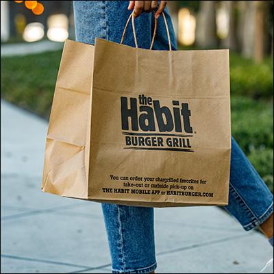 A brown paper bag "the Habit Burger Grill" on the side. A person walking, carrying it.