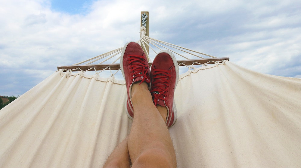 two feet with red shoes propped up in a hammock, a partly cloudy sky behind