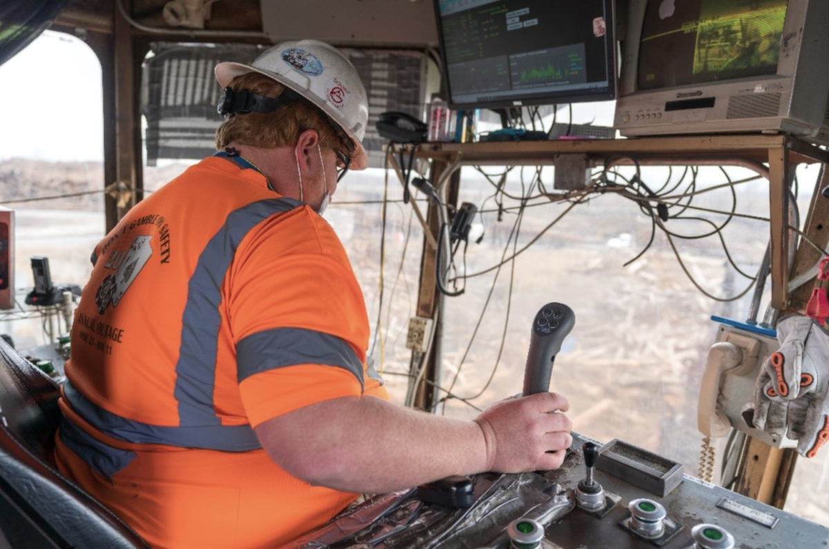 worker in a bright orange shirt and a hard hat at the controls of a large vehicle