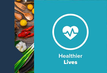 "Healthier lives" and logo. On the side a board of utensils, lobster, garlic and other produce.