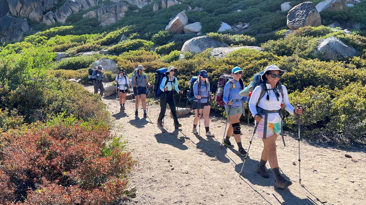 A line of hikers on a gravel path in mountainous terrain