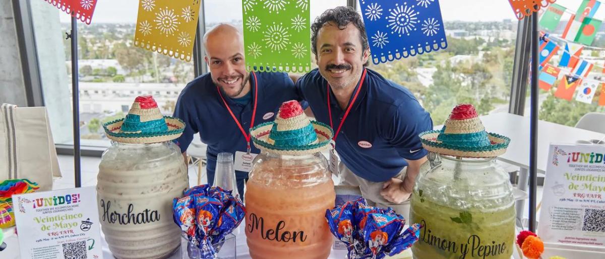 Two people smiling behind a table decorated and with three different drink dispenser