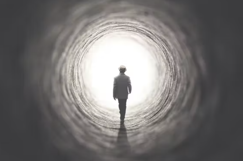 silhouette of person approaching the light at the end of a dark tunnel