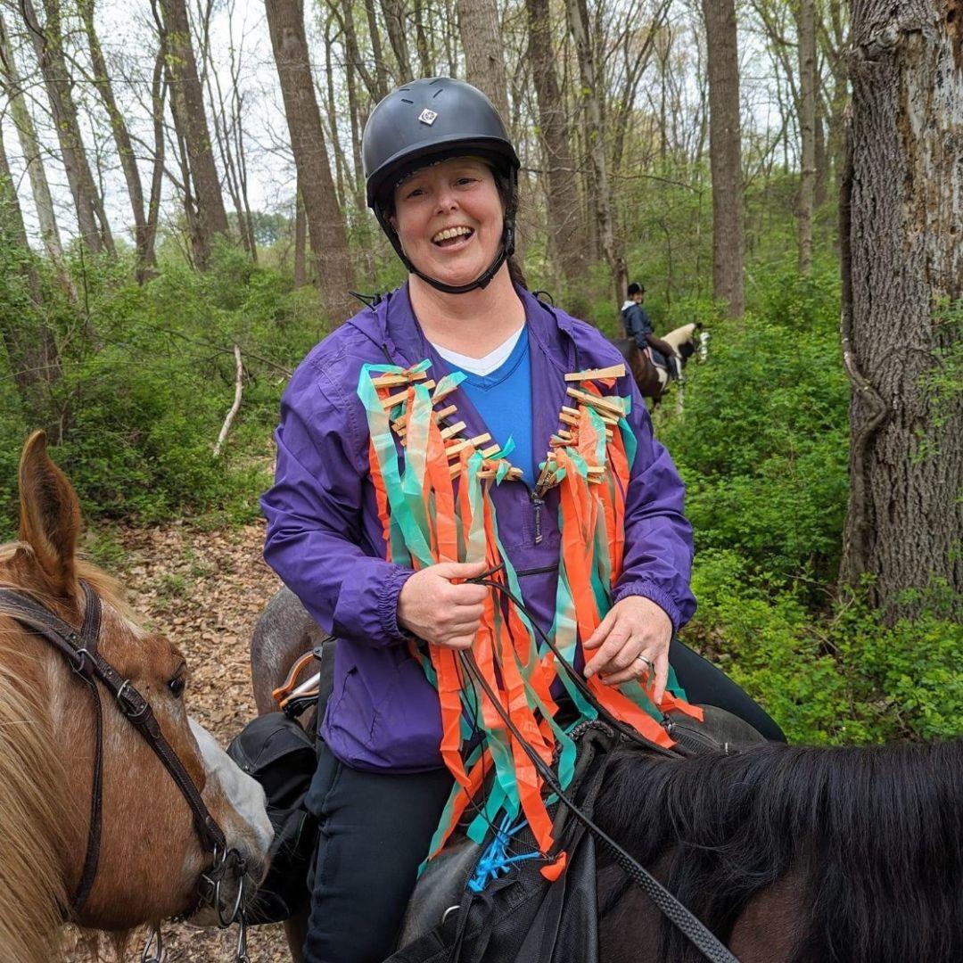 Julia Reilly riding a horse. Multiple colored strips on clothespins attached to her jacket.
