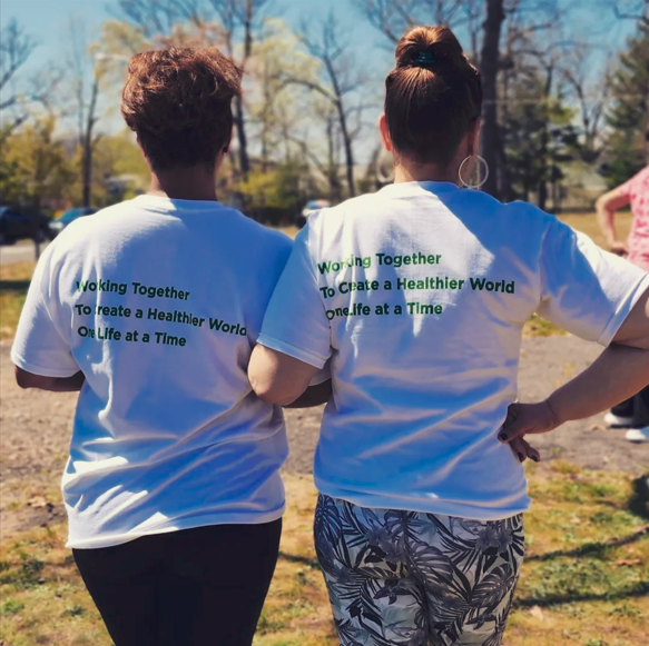 2 people with the same shirt pose with the back of shirt reads "working together to create a healthier world one life at a time."