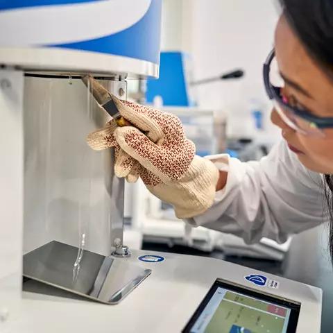 A person in protective lab wear using a scientific machine.