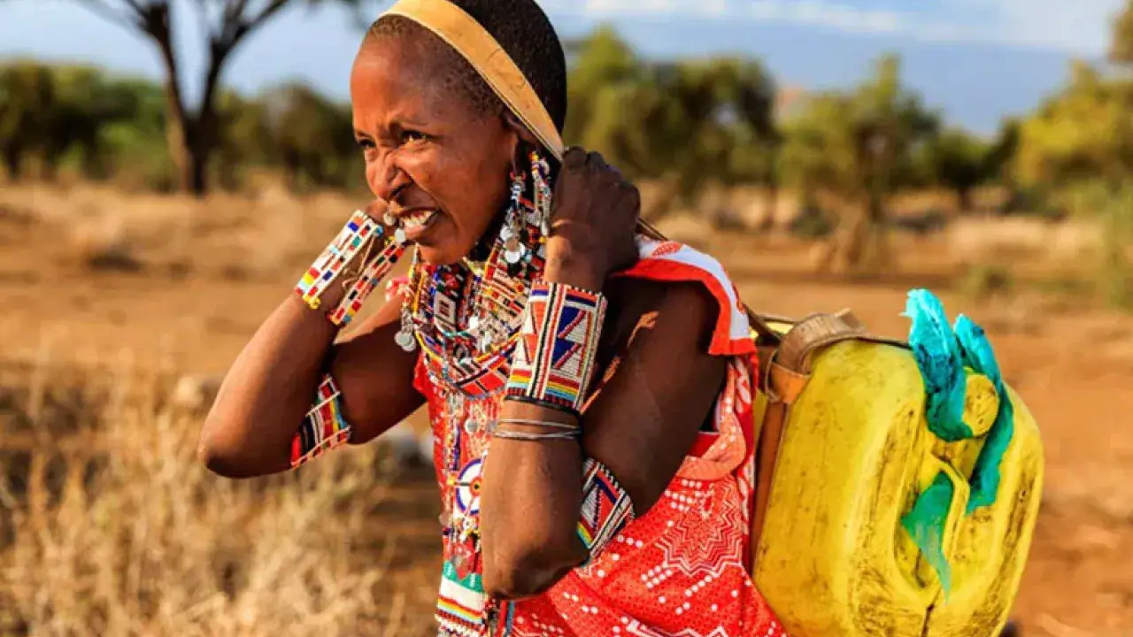 a person in Kenya, a water jug on their back with a strap around their head