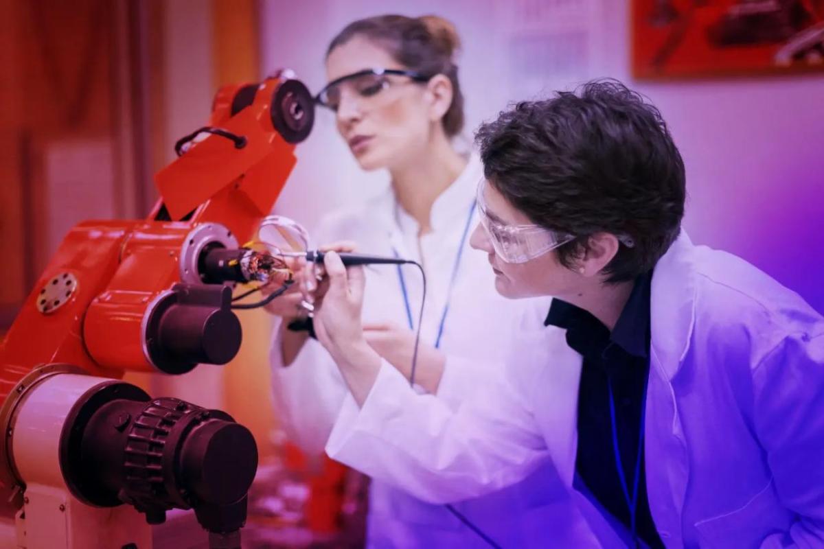 women in lab coats working on a piece of robotic equipment