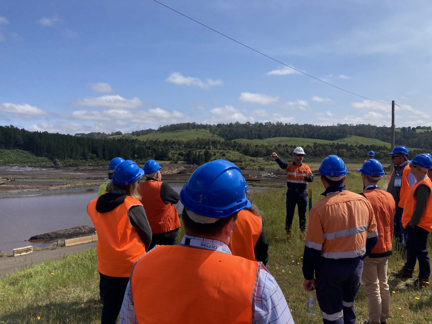 A group of people in hard hats and high-visibility safety vests visit a coal mining site. 