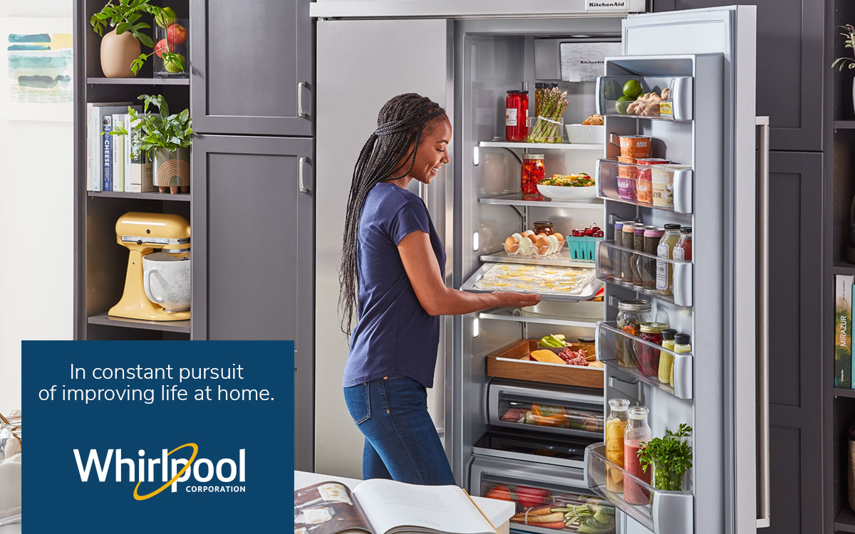 a person holding a pan of food in an open fridge. Whirlpool logo and "In constant pursuit of improving life at home" in the right lower corner.