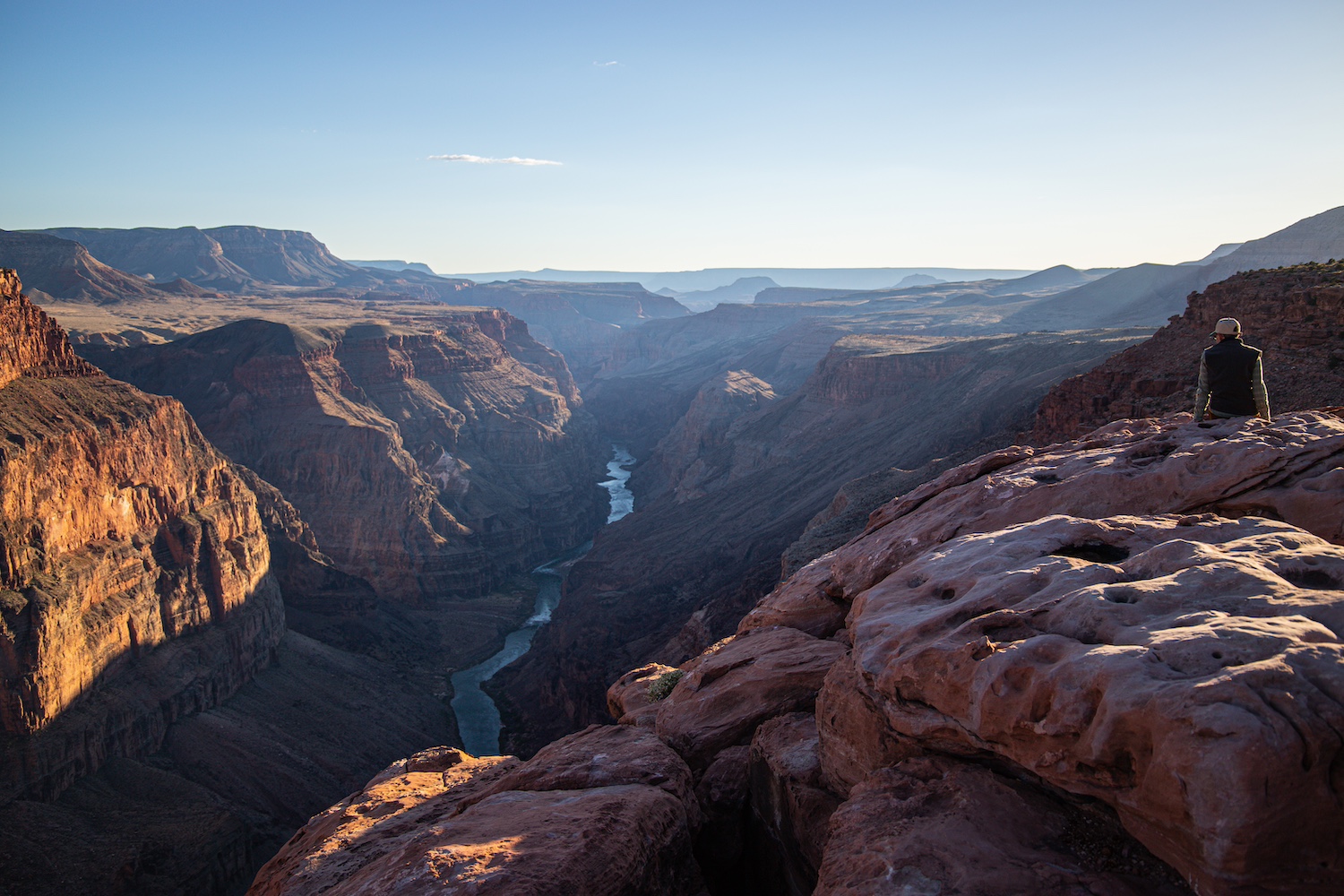A hiker sits at the top of the Grand Canyon watching the sunset — nationaparks