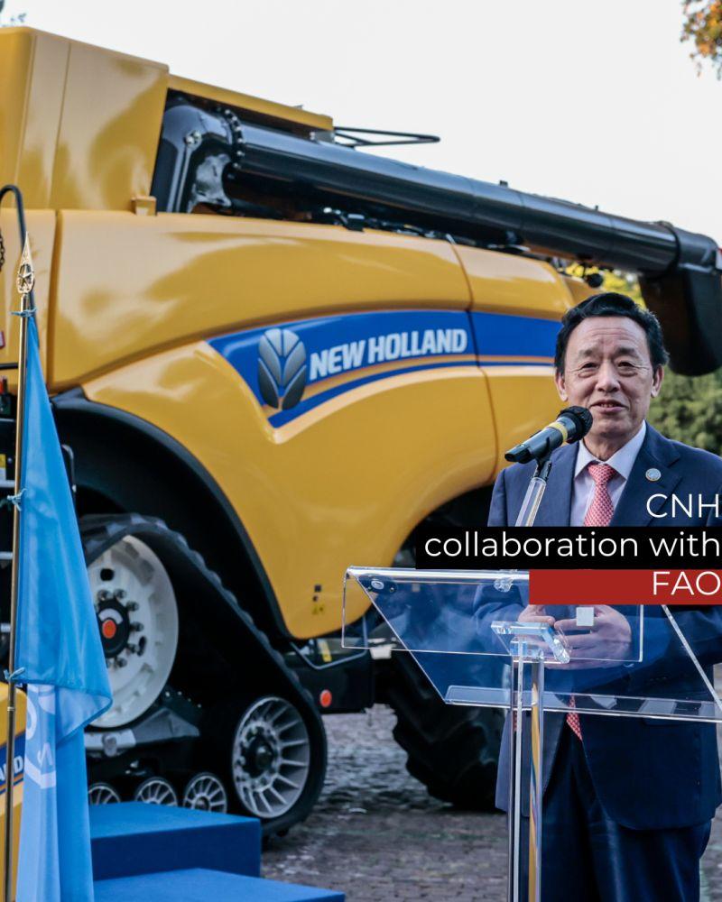 A person stood talking into a microphone near a yellow new holland tractor