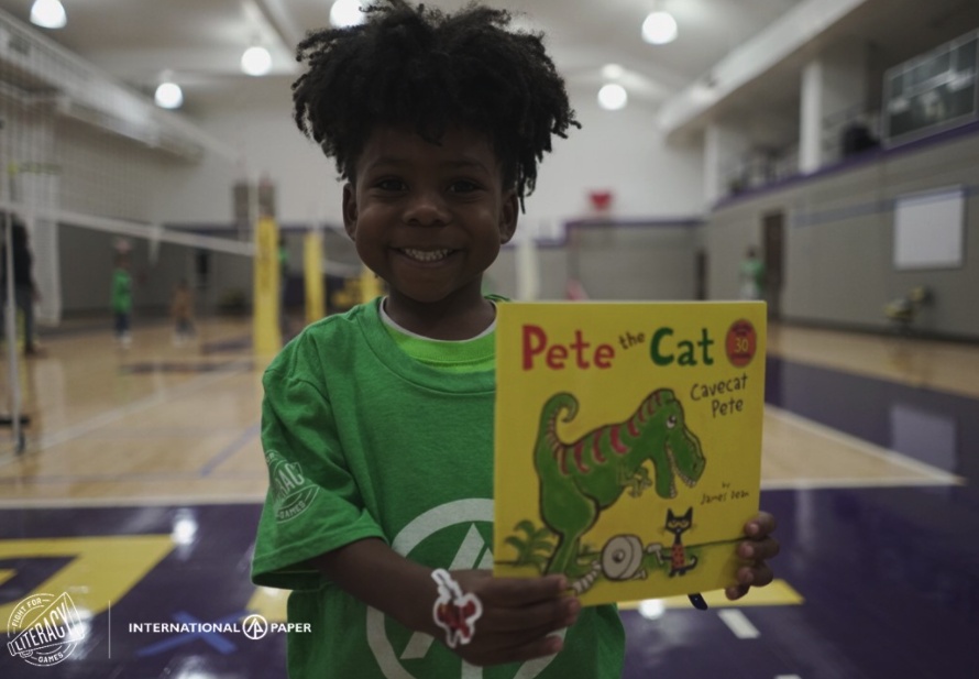 in a gym, a child with a big smile shows a book