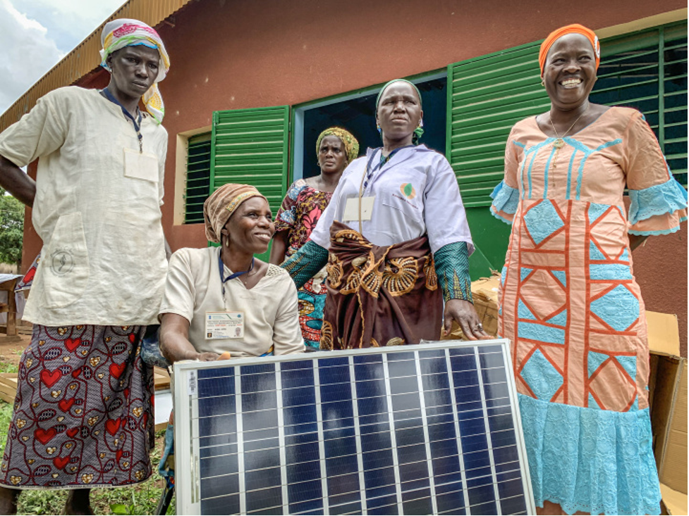Villagers in bright clothes pose with a solar panel