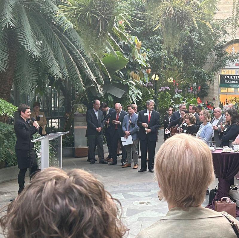 A group of people standing, listening to one speak at a podium.