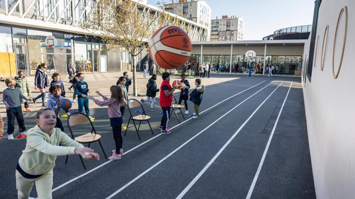 Children outside on a playground playing with basketballs and other equipment.