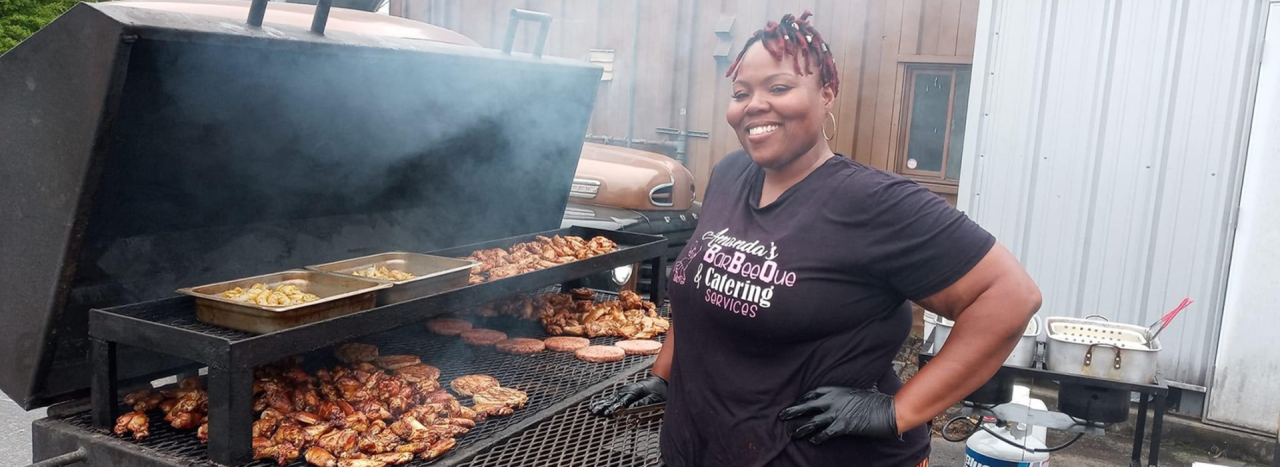 Amanda Kinsey-Joplin in a black t-shirt standing in front of a large barbecue smoker