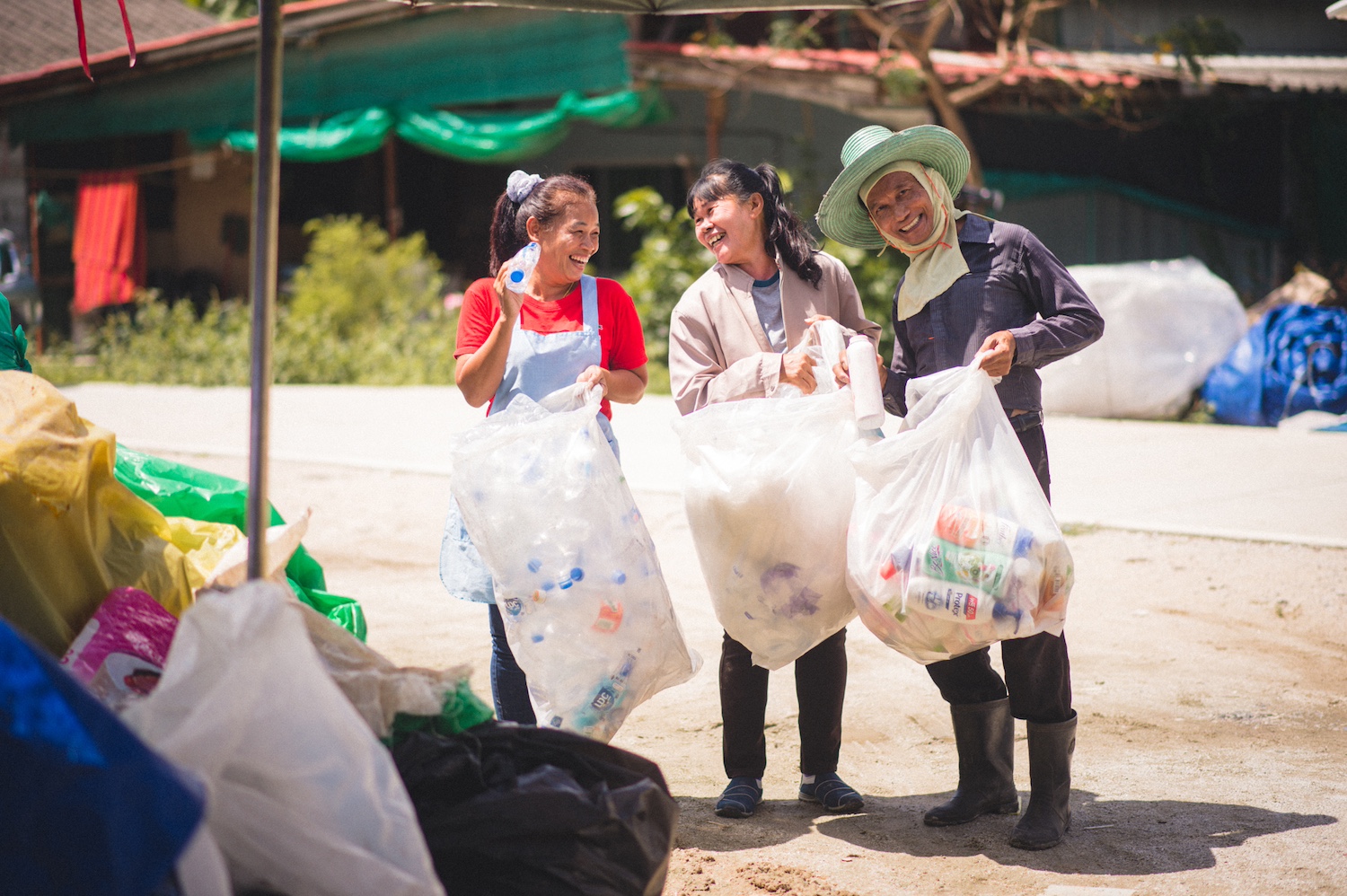 Three people collect post-consumer plastic bottles in large bags — plastic credits