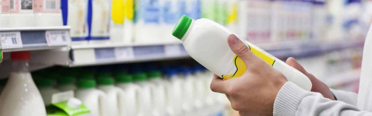 A person in a grocery store looking at a plastic container full of white liquid.