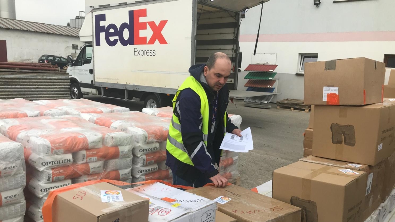 a person checks rows of boxes and wrapped pallets. A fedex truck behind them