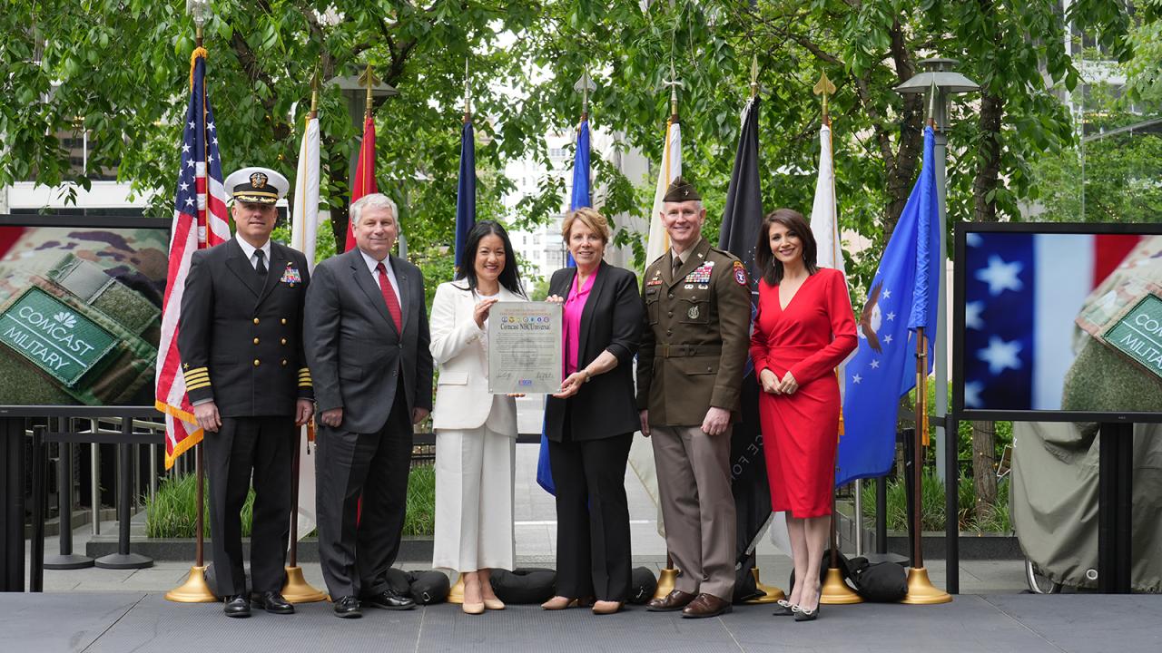 Comcast team members and members of the armed forces holding a document onstage at an event.