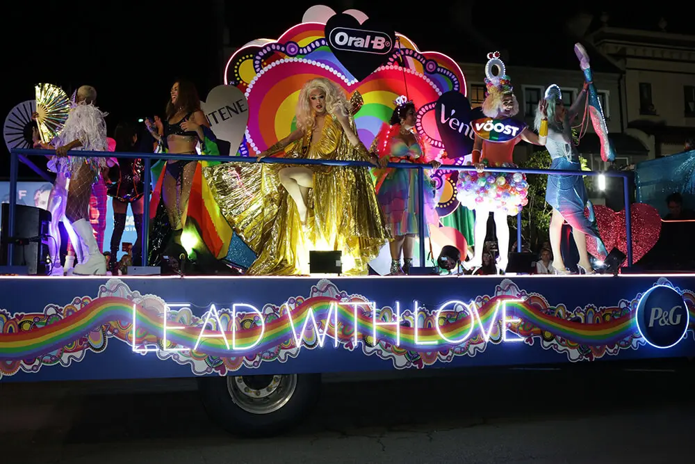 People riding on a pride float with glowing lights that read "Lead with love"