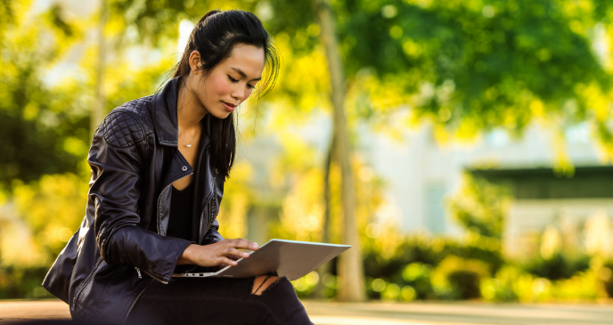 Image of a woman sitting on a park bench with her laptop