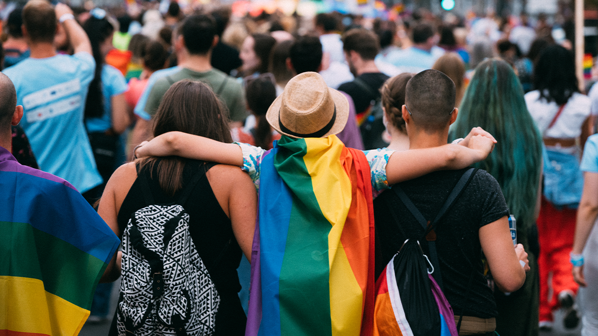 crowd with a person wearing a rainbow flag on their back