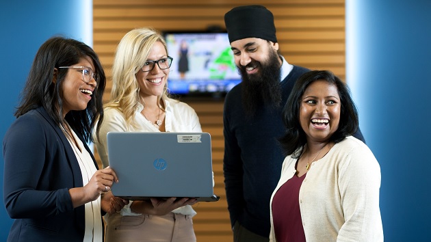 4 people look at a laptop smiling
