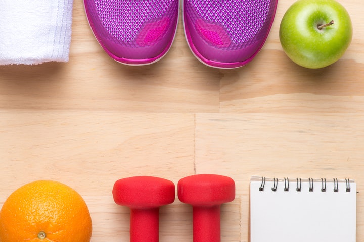 Sneakers, weights, and fruit next to a note pad on a hardwood floor