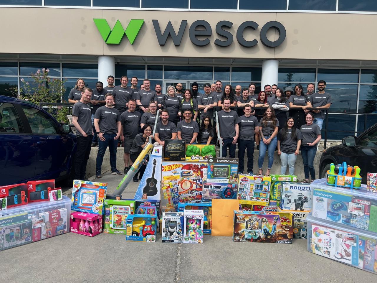 A group standing behind new toys, in front of a Wesco building
