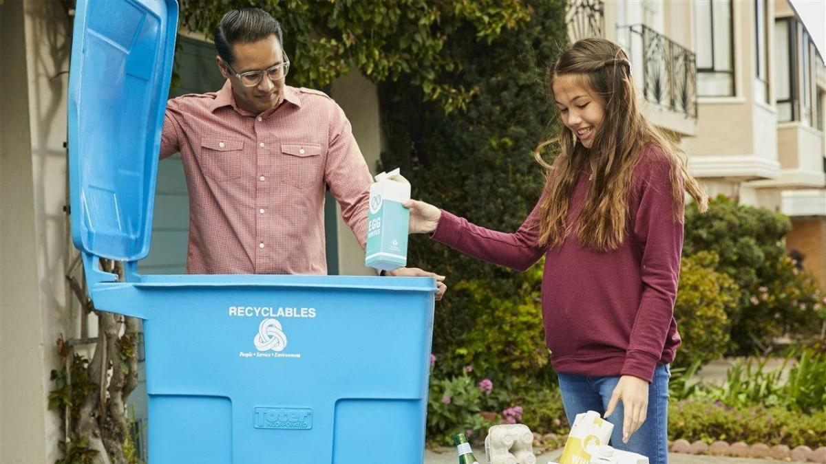 An adult and child putting items into a recycling bin.