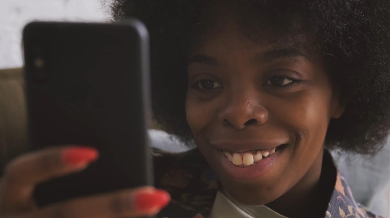 A smiling person looking at a cell phone they're holding in front of them.