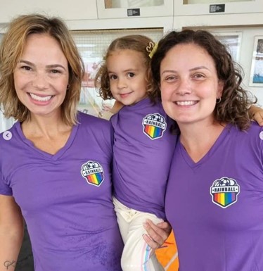 Renata (R), her partner Caru and their daughter Bia, wearing their Rainball team shirts.