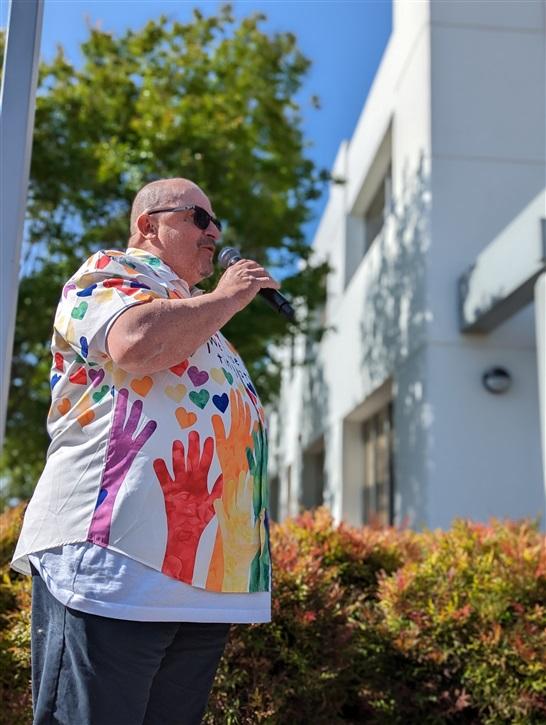 Rene Spring in a colorful handprint shirt speaking outside with a microphone.