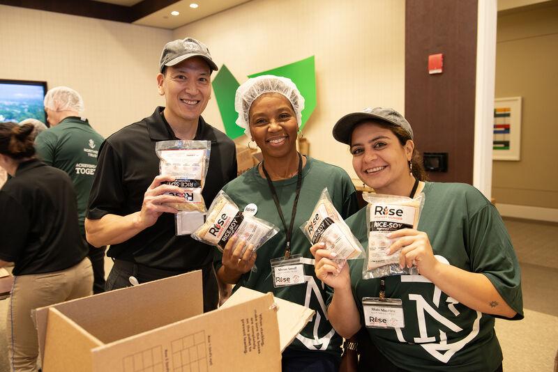 Three smiling volunteers posed, holding "RISE" packs.