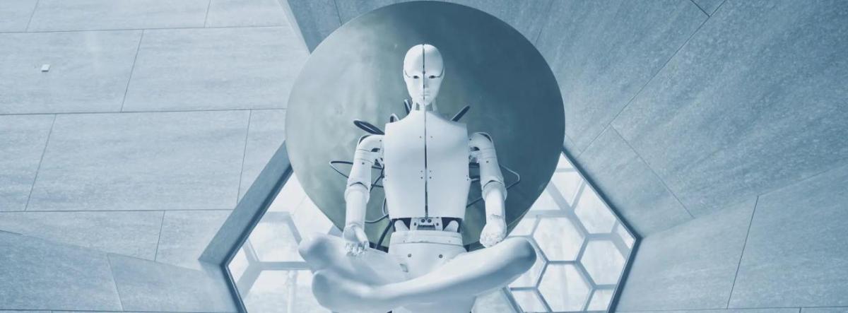 A white human-like robot sitting cross-legged in a stark room of geometric shaped windows and walls.