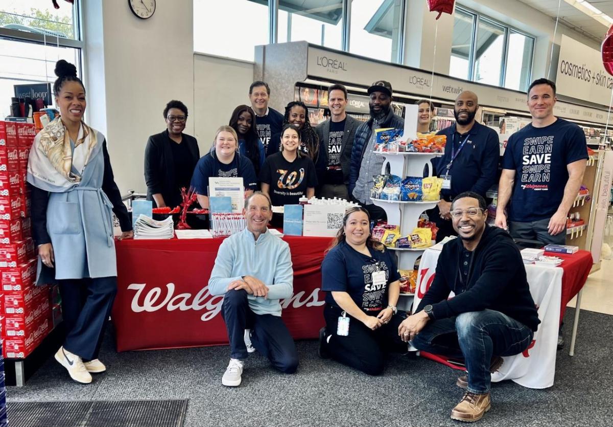 A group of people posed inside a Walgreens by a decorated table with treats and pamphlets.