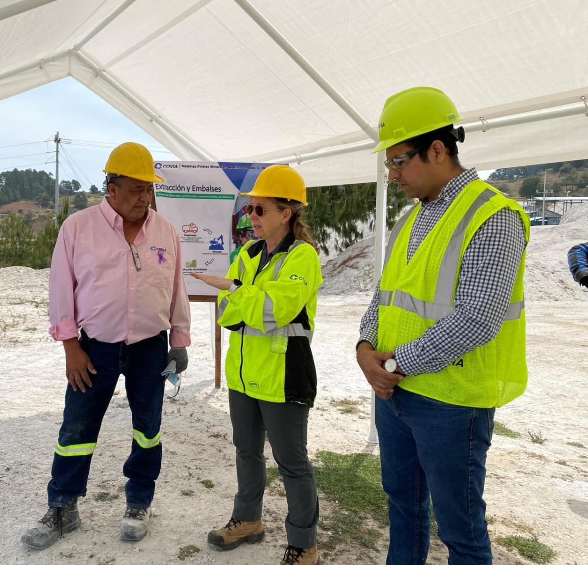 Three people talking under a canopy, each wearing hard hats and high-vis clothing.