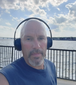 scott cabral wearing headphones, a railing and waterway behind him