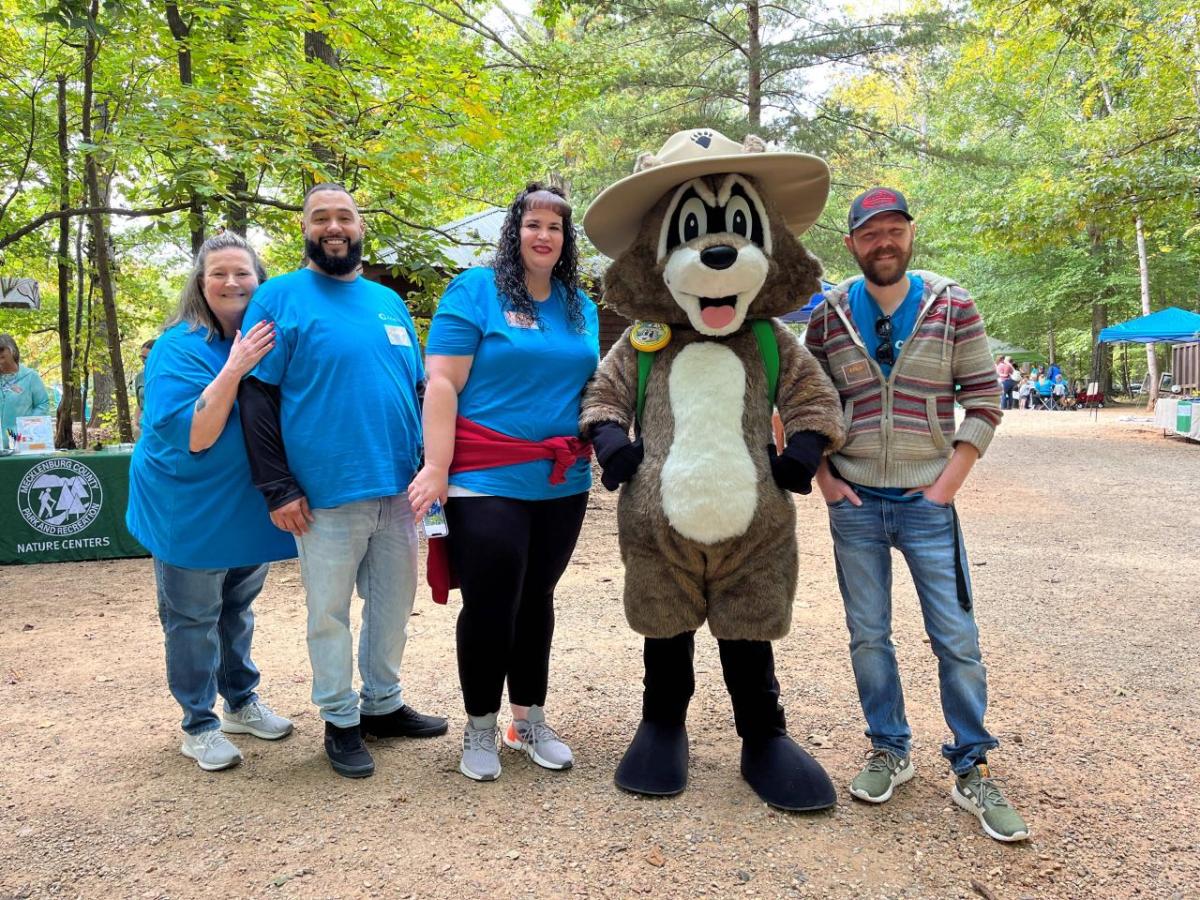 Four people and a mascot pose smiling for the camera outdoors.