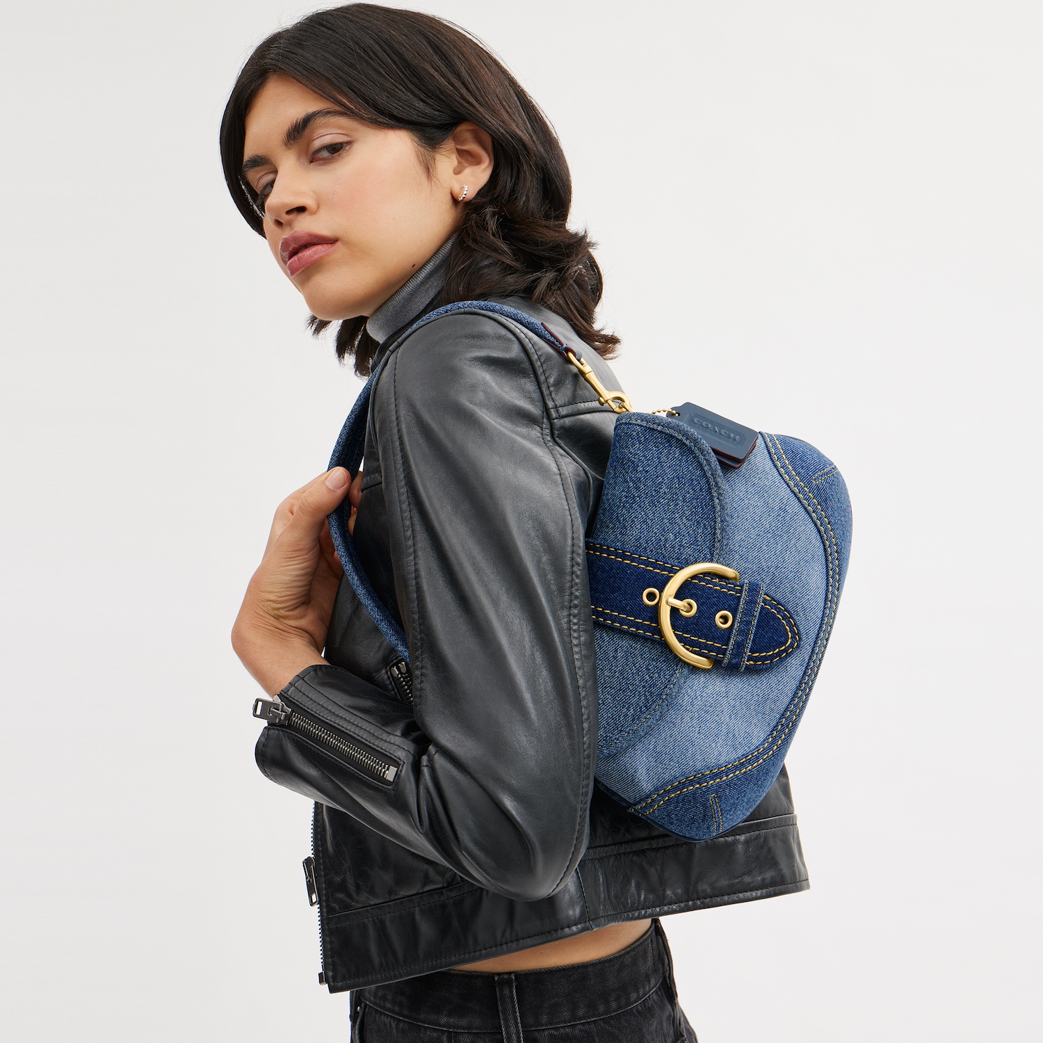 A model holds the Coach Soho Bag made of repurposed denim over their shoulder.