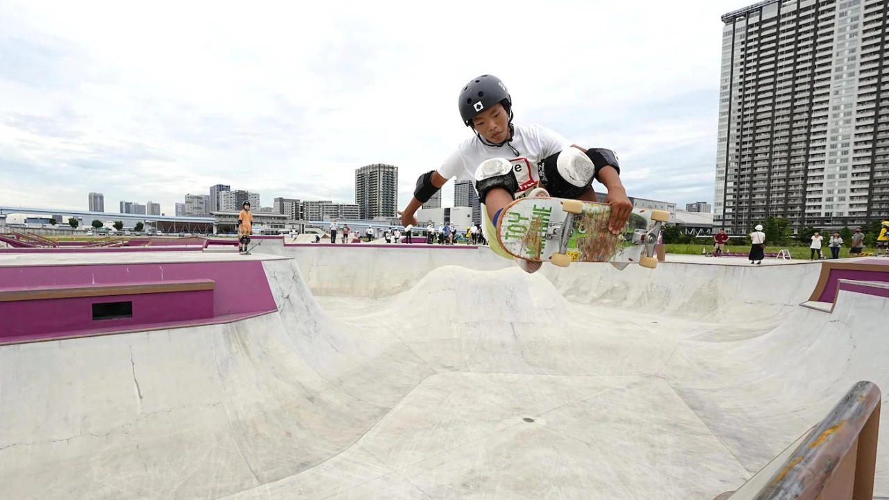a skateboarder doing a trick in a cement skate park, tall buildings in the background