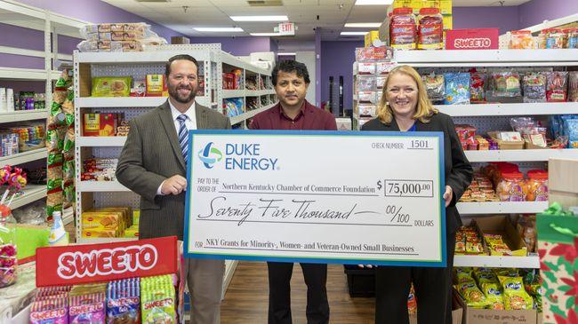 Three people in a small grocery store holding a large check.