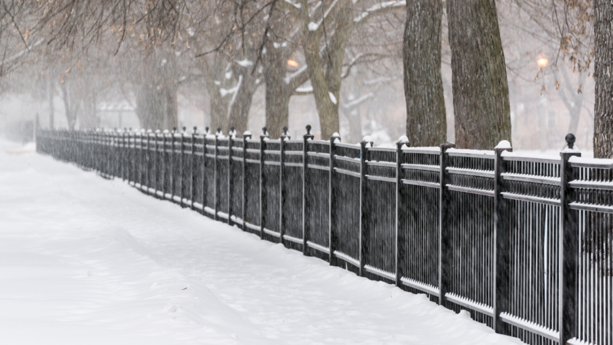 A black fence alongside a snow covered walkway.